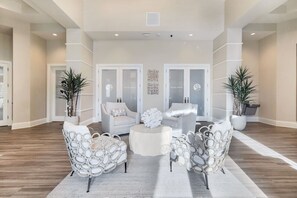 Een ruime woonkamer met een lichtkleurige bank, twee gestreept fauteuils, een ronde salontafel en twee potplanten.