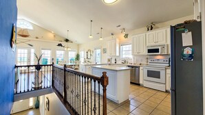 A spacious kitchen with white cabinets, a central island, a refrigerator, and a microwave. - Dive into "Summer Days & Cooler Nights"! w/ pool! (Surf City)