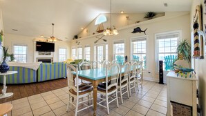 A spacious kitchen with a dining area, featuring a large table, white chairs, and a ceiling fan. - Dive into "Summer Days & Cooler Nights"! w/ pool! (Surf City)
