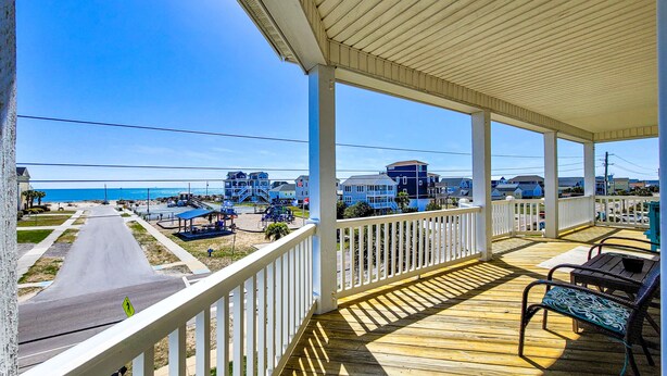 A covered outdoor area with a view of the beach and buildings in the background. - Dive into "Summer Days & Cooler Nights"! w/ pool! (Surf City)
