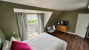 A bedroom with a bed, a dresser, a TV, and a window with curtains. - Maison Du Havre (Petit Duplex) (La Malbaie)