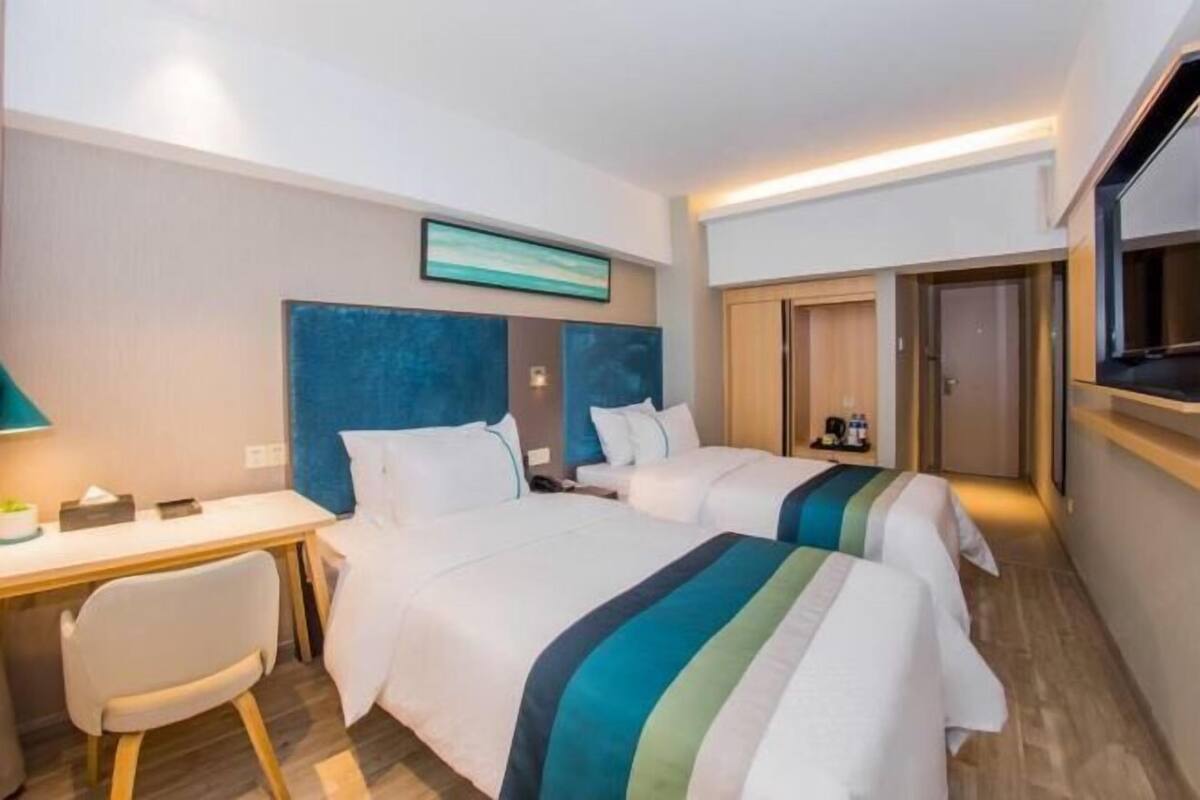 A hotel room with two beds, a desk, a chair, a TV, and a painting on the wall.