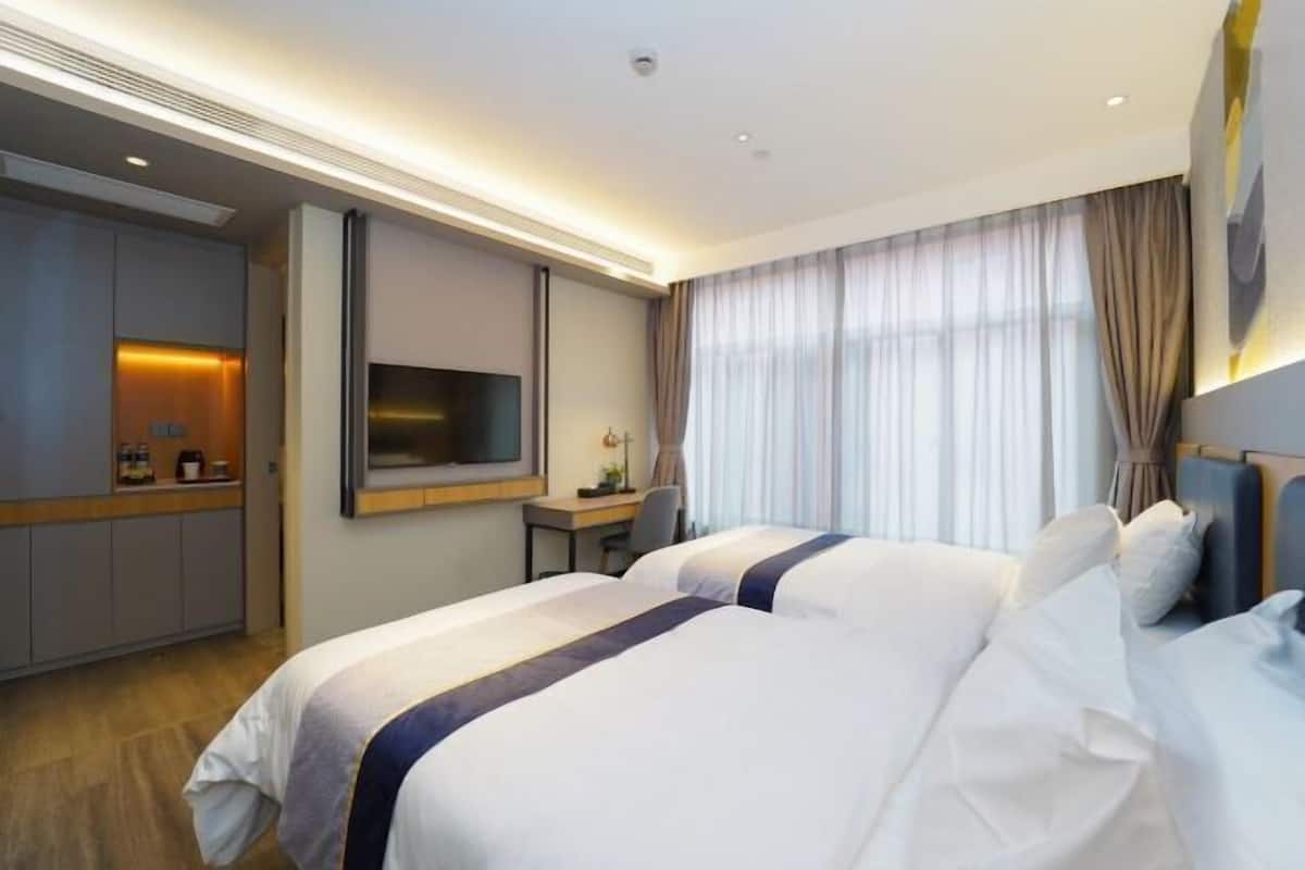 A hotel room with two beds, a desk, a TV, and a minibar.