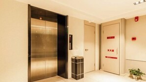 Un ascenseur dans un couloir, avec une poubelle à côté.