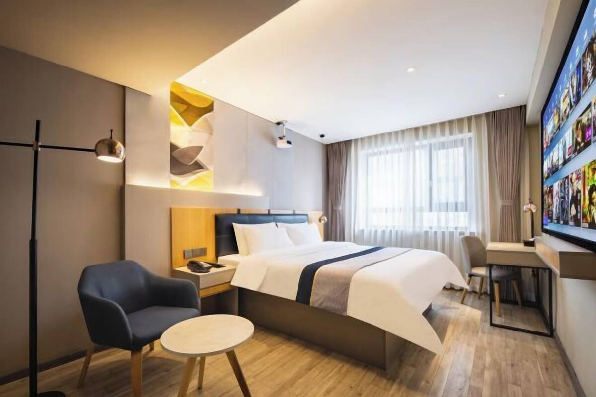 A modern hotel room with a bed, a desk, a chair, and a small table.