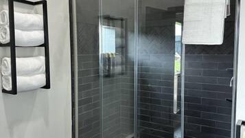 A modern bathroom with a glass shower enclosure, black tiled walls, and a towel rack with folded towels.