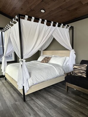 A four-poster canopy bed with white bedding and a zebra-patterned pillow, wooden headboard, and a dark wooden bench with a striped pillow.