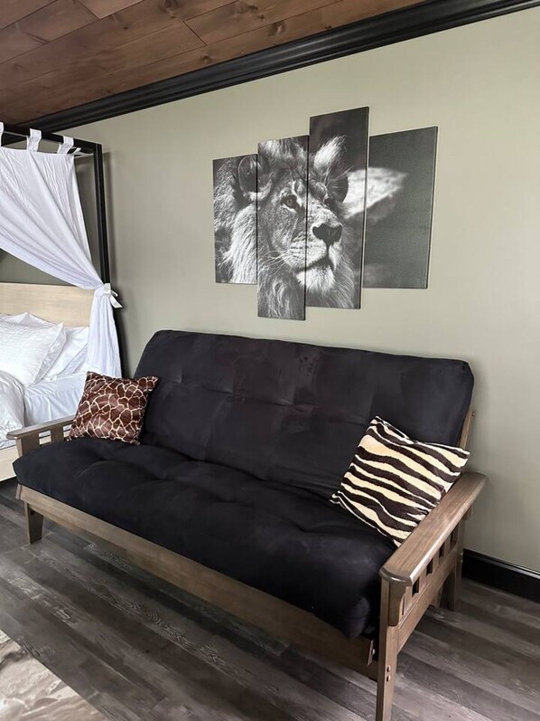 A black sofa with two pillows, a white canopy, and a wall with a lion print.