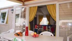 A dining area with a table set for two, a red vase, and a fruit bowl.