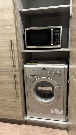 Un appareil compact combinant lave-linge et sèche-linge, doté d’un panneau de commande numérique et logé dans un meuble en bois muni d’une poignée.