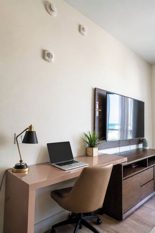 Un espace de bureau moderne comprenant un bureau, un ordinateur portable, une chaise et un grand téléviseur à écran plat.