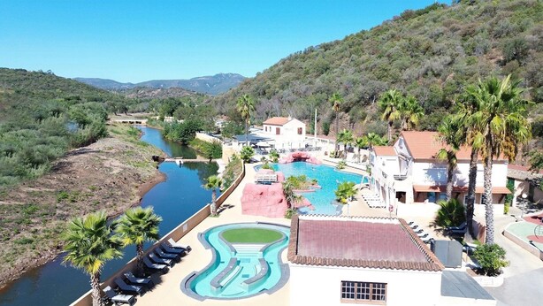 Ein Resort mit großem Schwimmbad, einem Fluss und bergigem Hintergrund.