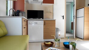 Eine kompakte Küche mit Geschirrspüler, Mikrowelle und kleinem Kühlschrank. Ein Essbereich mit Tisch für zwei Personen, auf dem eine Schüssel Chips und zwei Getränke mit Trinkhalmen stehen.