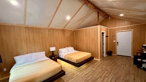 Een slaapkamer met twee bedden, houten wanden, een schuine plafond en een deur naar een andere kamer.