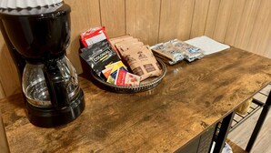 Een koffiezetapparaat, een dienblad met koffiekapsules en een zak koffie op een houten tafel.