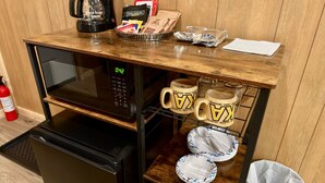 Een kleine keuken met een magnetron, koffiezetapparaat en opbergruimte voor koffie en snacks.