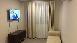 A room with a television mounted on the wall, a dark wooden cabinet, and a beige sofa.