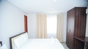 A hotel room with a bed, a wardrobe, and a window with curtains.