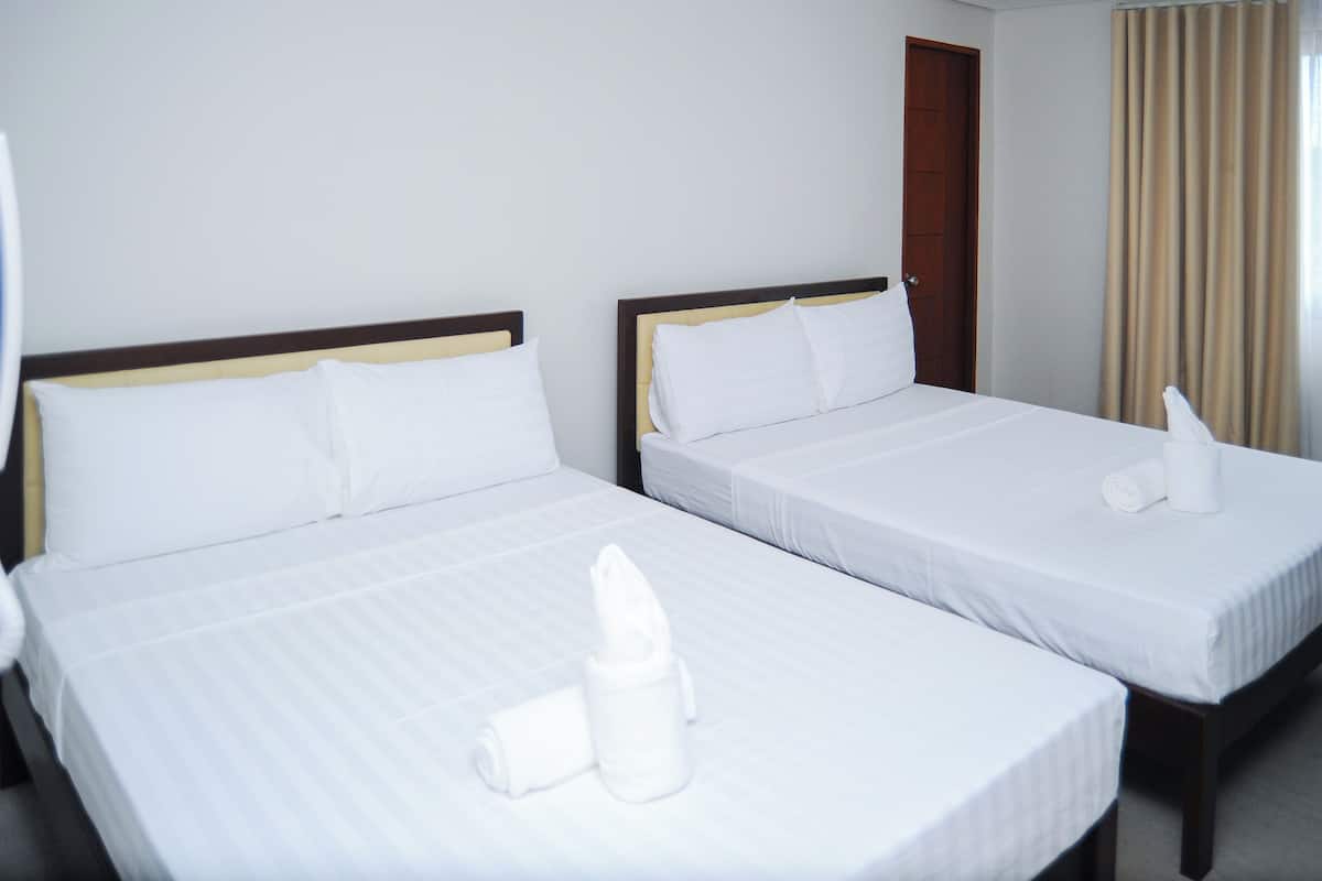 Zwei Einzelbetten mit weißer Bettwäsche, ein hölzerner Kopfteil und ein gerolltes Handtuch auf jedem Bett.