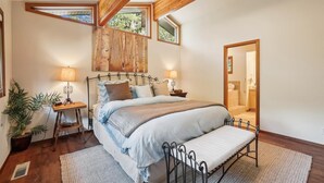 A bedroom with a large bed, two bedside tables with lamps, a wooden ceiling, and a view of the bathroom through an open door. - Stunning Peak Views-Spacious Bear Creek 4Bdrm Home (Alpine Meadows)