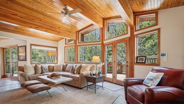 A spacious living room with a wooden ceiling, large windows offering a view of the outdoors, a leather sofa, a coffee table, and a red armchair. - Stunning Peak Views-Spacious Bear Creek 4Bdrm Home (Alpine Meadows)