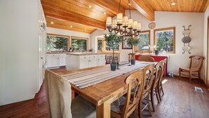 A spacious kitchen with wooden ceiling beams, a central island with chairs, and large windows offering a view of the outdoors. - Stunning Peak Views-Spacious Bear Creek 4Bdrm Home (Alpine Meadows)