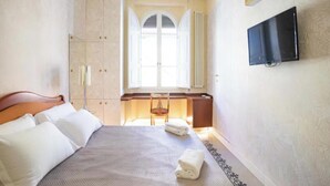 Una habitación de hotel con cama, escritorio, silla, televisor y ventana con contraventanas.