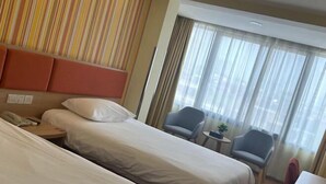 A hotel room with two beds, a small table, a chair, and a window with curtains.