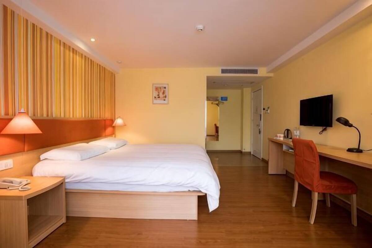 A hotel room with a bed, desk, chair, TV, and a door leading to another room.