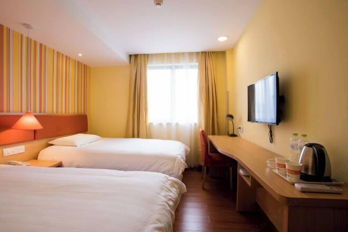 A hotel room with two beds, a desk, a chair, a television, and a window with curtains.