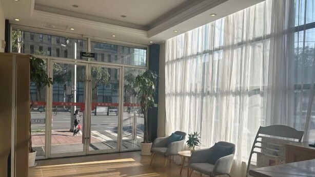 A spacious lobby with large windows, a wooden floor, and a seating area with chairs and a table.