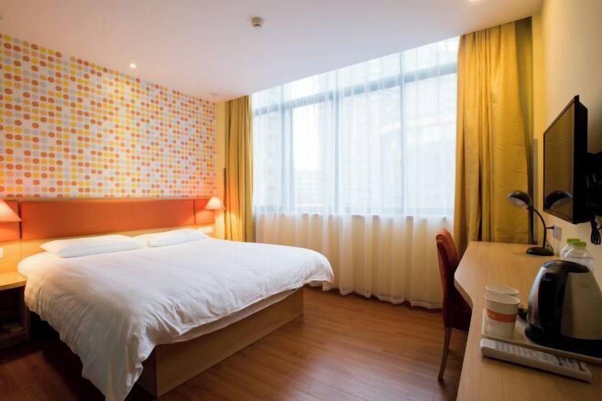 A hotel room with a bed, a desk with a chair, a television, and a window with curtains.