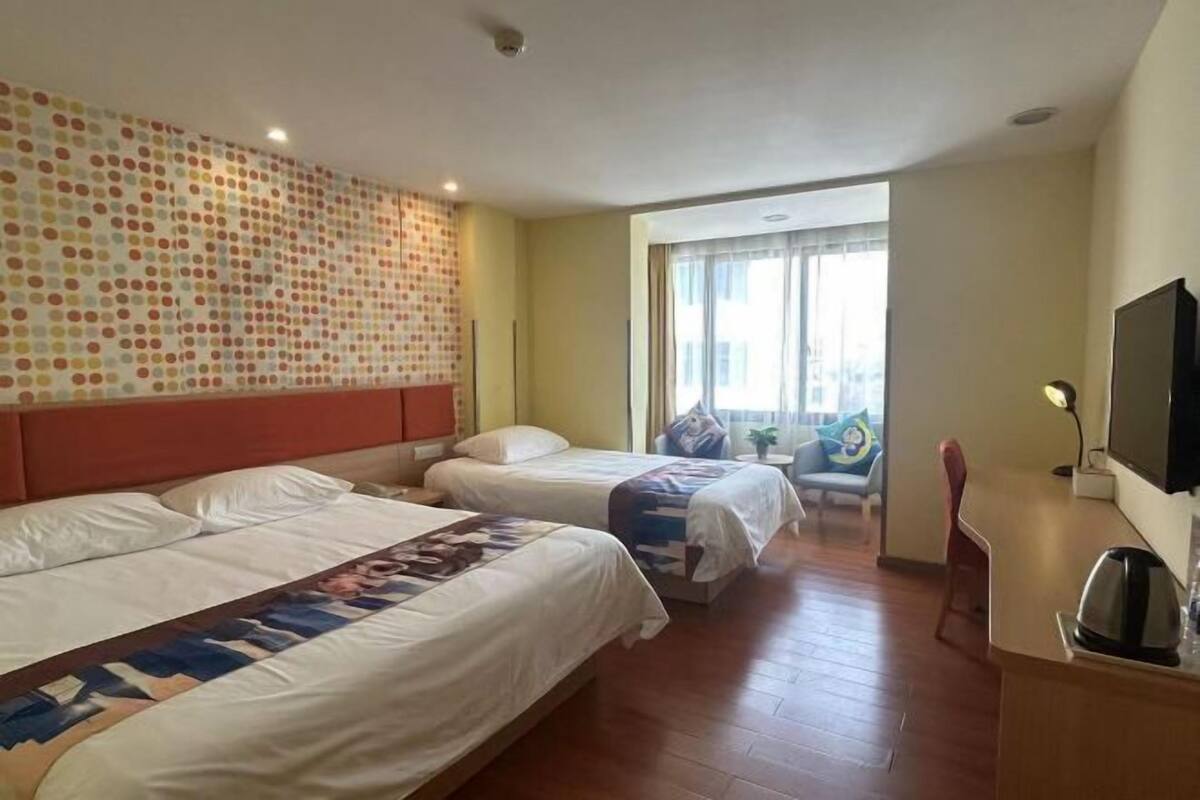 A hotel room with two beds, a TV, a desk, and a large window.