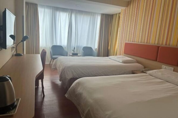 A hotel room with two beds, a desk with a lamp, a chair, a small table, and a window with curtains.