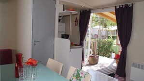 Un comedor con una mesa dispuesta para dos comensales, un florero rojo y un frutero.