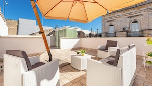 Eine Dachterrasse mit Korbmöbeln, einem großen Sonnenschirm und Blick auf ein historisches Gebäude.