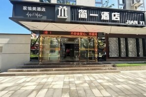 Entrada de hotel con fachada de vidrio, un letrero con caracteres chinos y pavimento adoquinado.