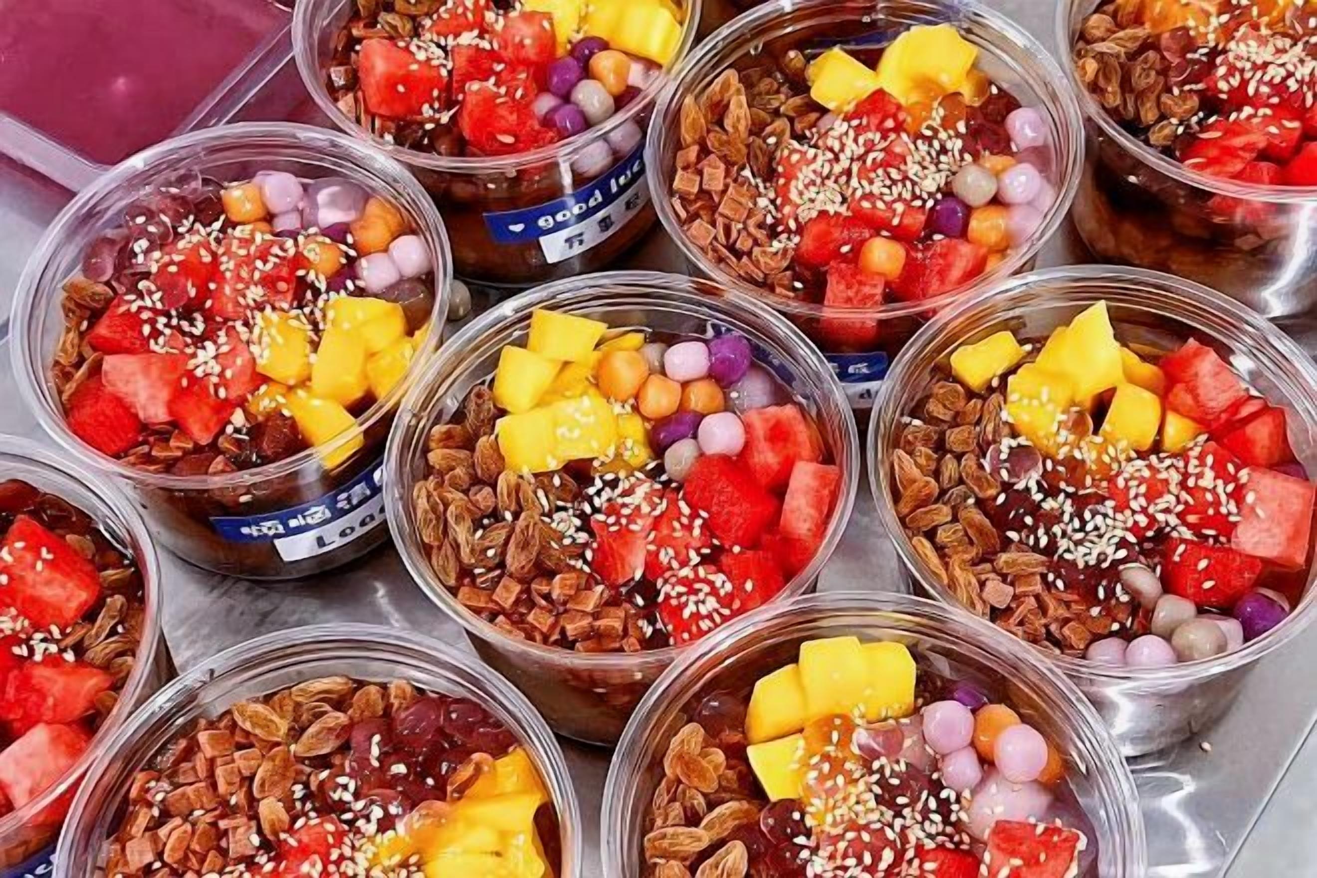 Multiple clear plastic cups filled with a variety of fruits, nuts, and other toppings.
