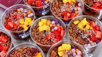 Multiple clear plastic cups filled with a variety of fruits, nuts, and other toppings.