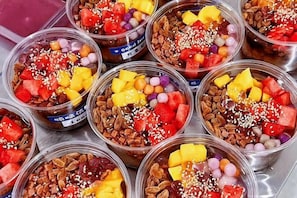 Varios vasos de plástico transparente llenos de frutas, nueces y otros ingredientes.
