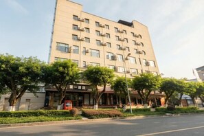 A multi-story hotel with a flat facade, air conditioning units, and a well-maintained front garden with trees and shrubs. - Chongqing Jiayumei Hotel (Chongqing)