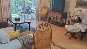 Ein Wohnzimmer mit einer Couch, Sesseln, einem Couchtisch, einem Fernseher und einem Essbereich mit Stühlen und einem Tisch.