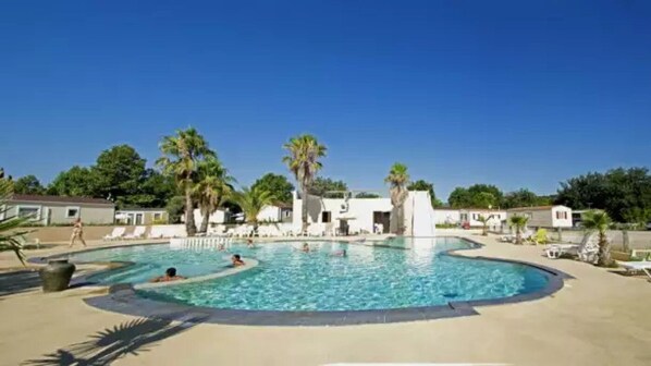 Una piscina de borde curvo, rodeada de sillas de descanso y palmeras.