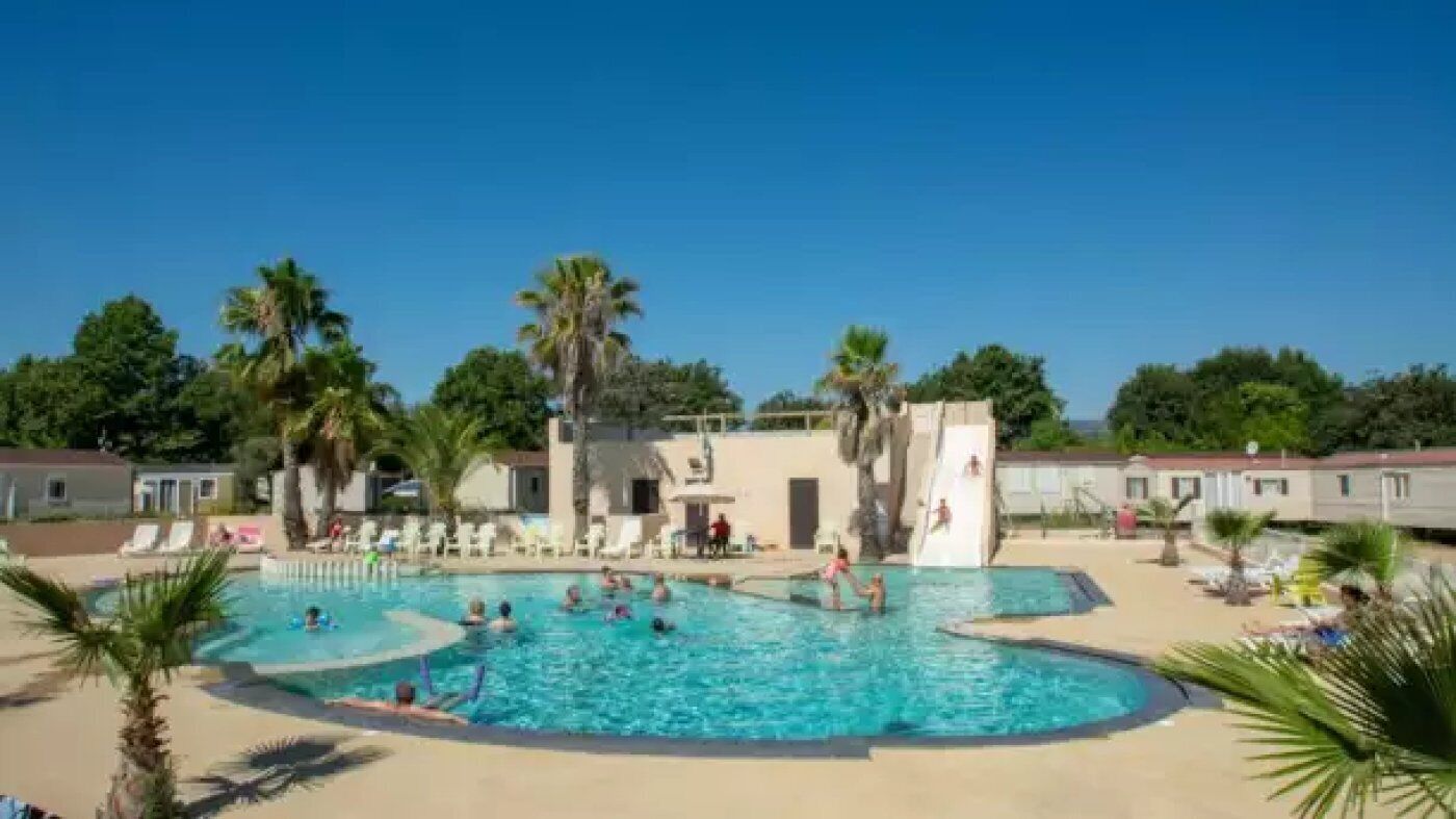 Zona de piscina con varias piscinas, palmeras y sillones de descanso.