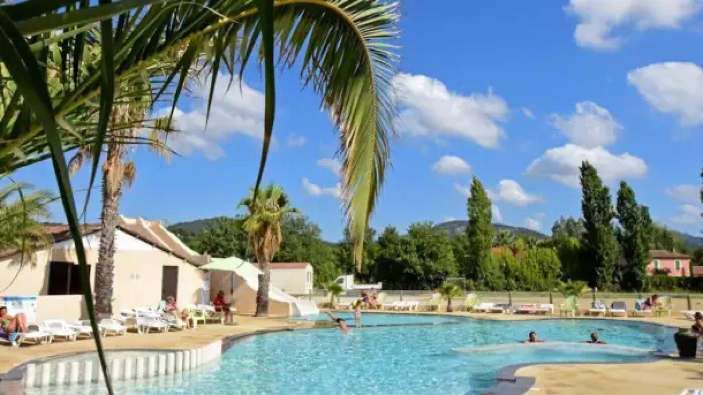 Una piscina con sillas de descanso y palmeras, rodeada de edificios y colinas.