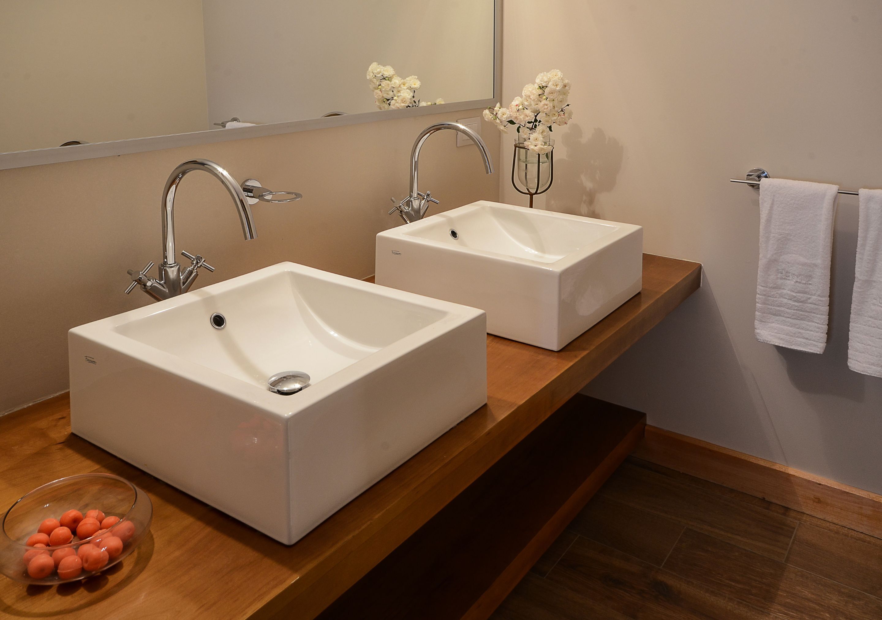 Un baño con dos lavamanos blancos, un espejo, una encimera de madera y un perchero para toallas.