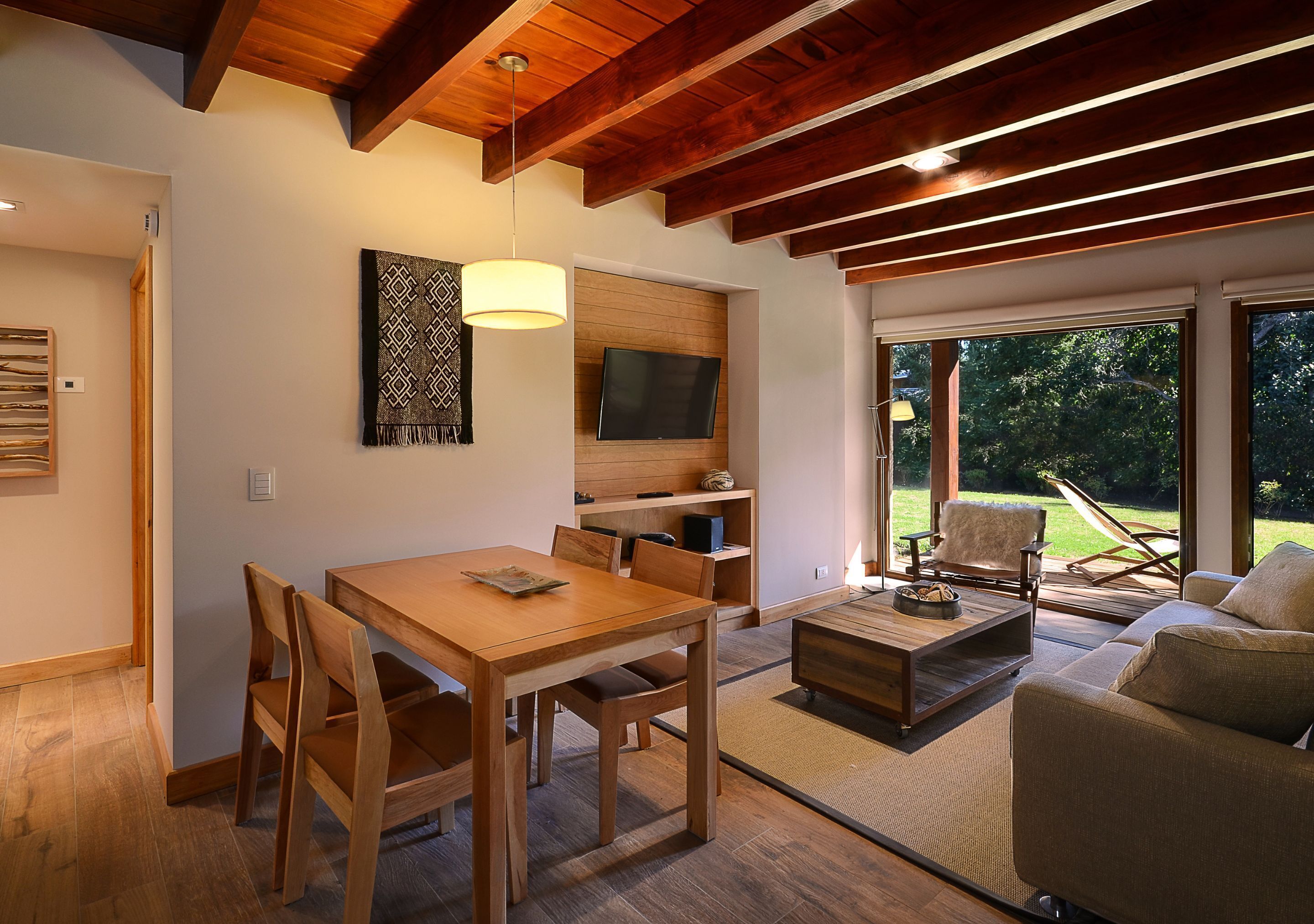 Una sala de estar moderna con una mesa de comedor de madera, sillas, un sofá y un televisor montado en una pared de madera.