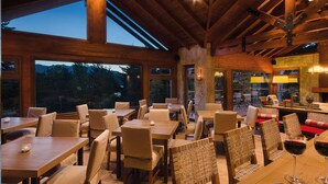 Een restaurant met houten tafels en stoelen, grote ramen en een stenen pilaar.