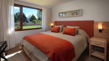 A bedroom with a large bed, a nightstand, a wooden dresser, a window with curtains, and a view of the outdoors.