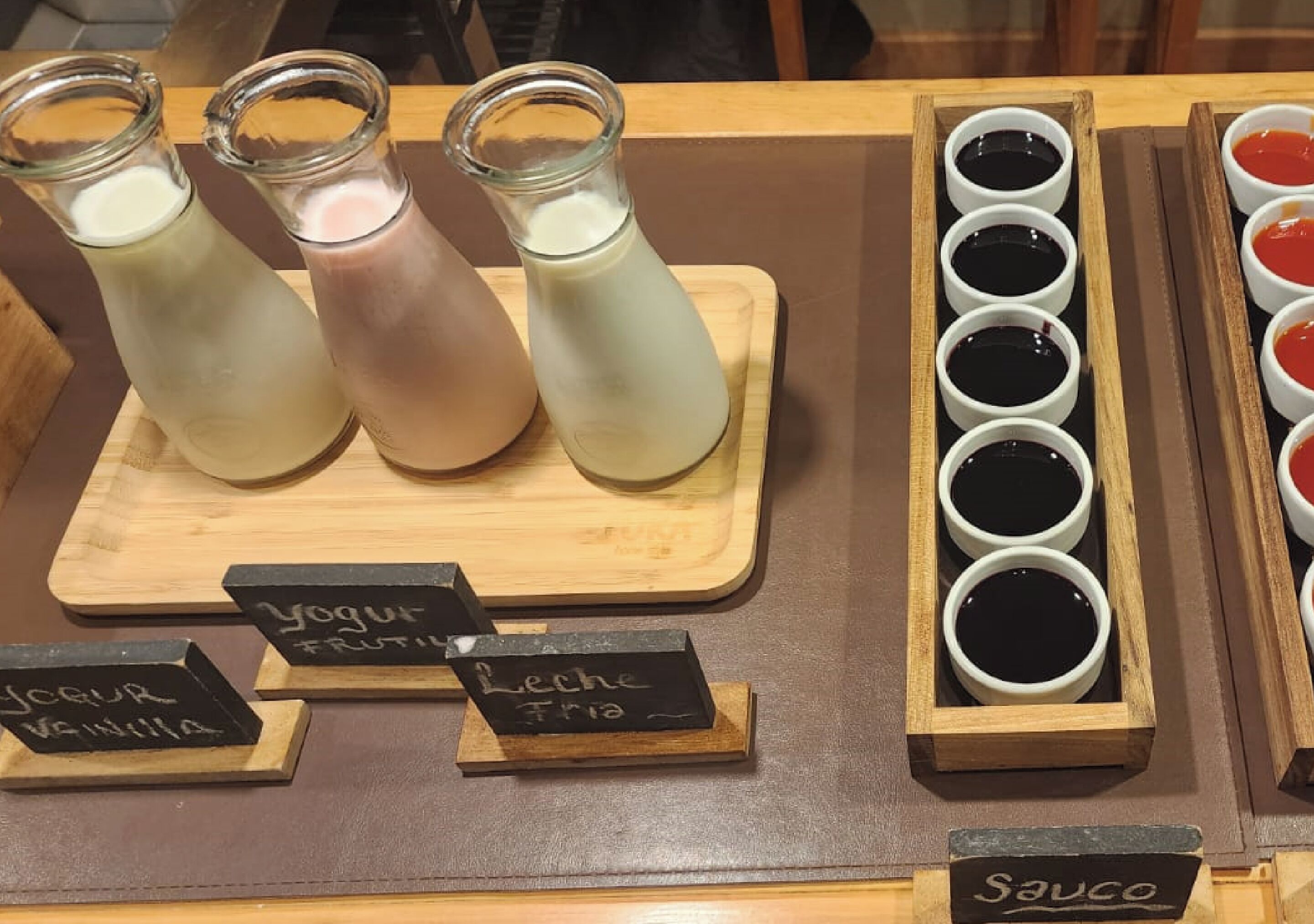 Un présentoir de boissons avec trois bouteilles de lait et divers contenants étiquetés, notamment des yaourts et des sauces.